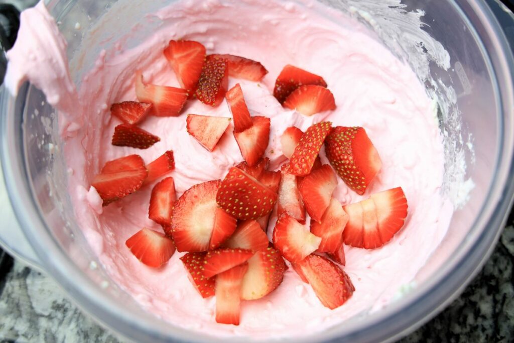 strawberry cheesecake dip in a plastic bowl with fresh strawberries.