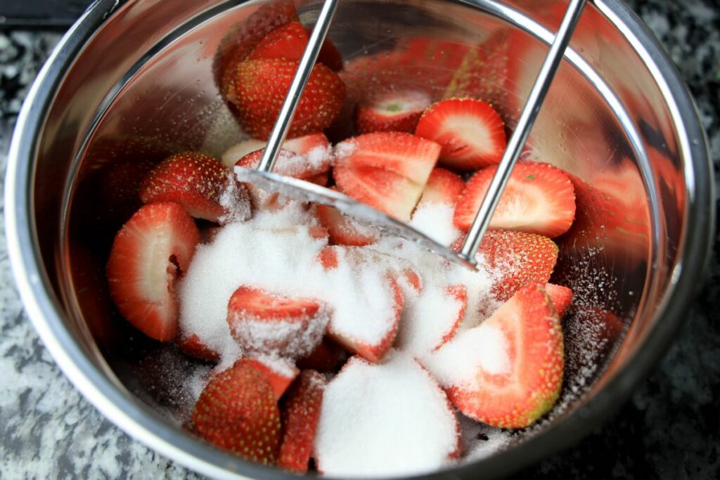 Sliced strawberries with sugar on top in a metal bowl with a masher.
