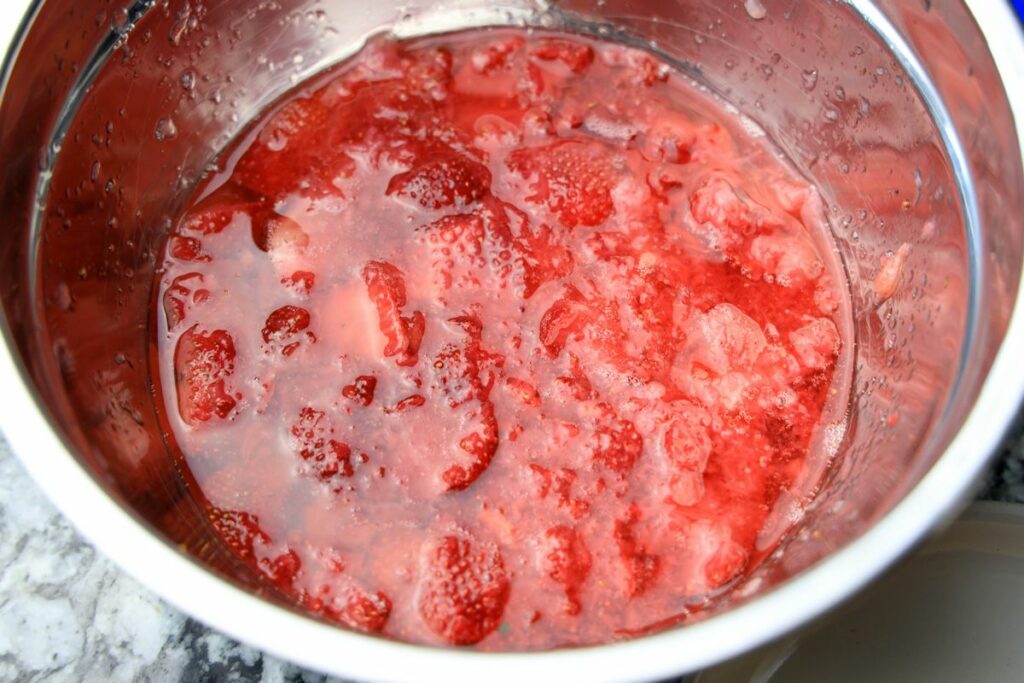 Strawberries in a sugared syrup in a metal bowl.