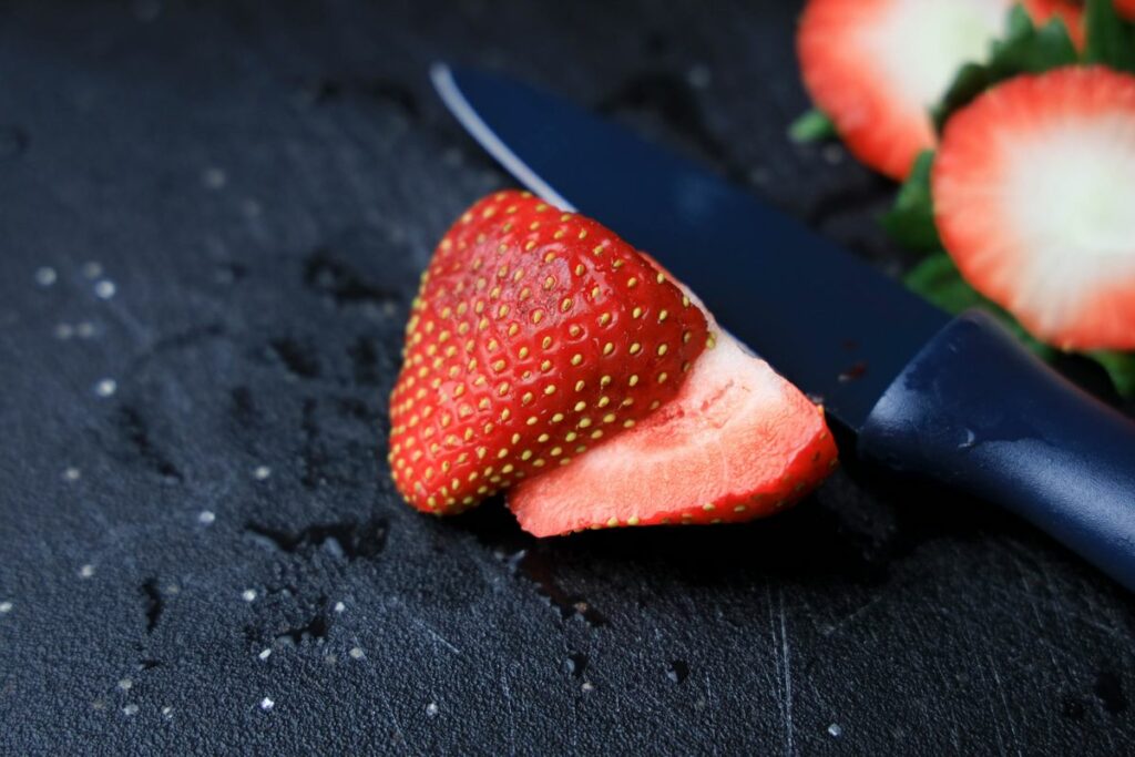 Strawberry sliced on a black cutting board.