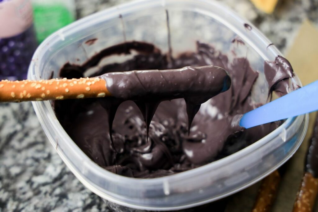 Black candy melts melted in a bowl with a dipped pretzel rod.