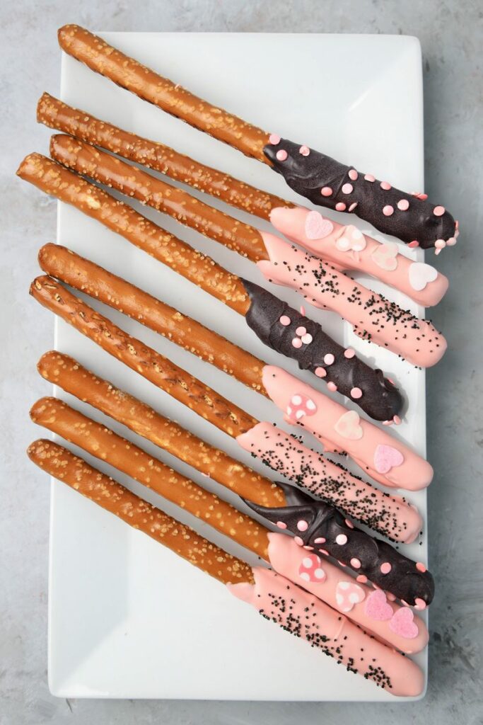 Valentine's Day Pretzel Rods on a white plate on a faux concrete backdrop.