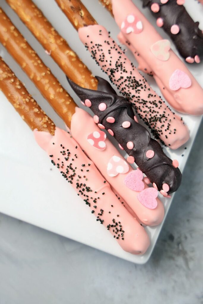 Valentine's Day Pretzel Rods on a white plate on a faux concrete backdrop.