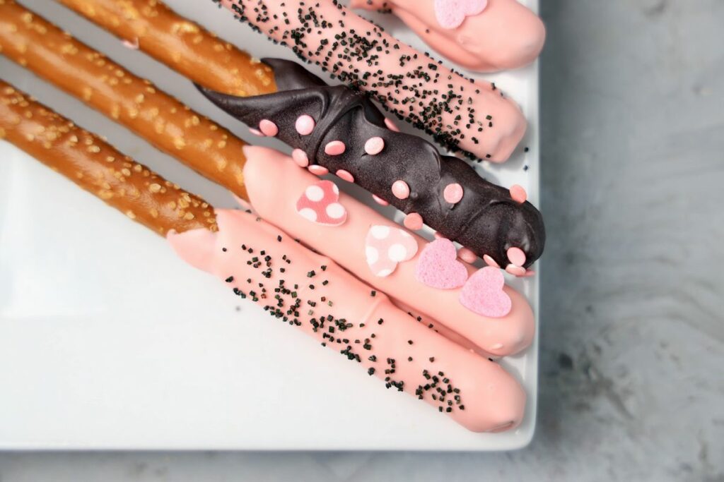 Valentine's Day Pretzel Rods on a white plate on a faux concrete backdrop.