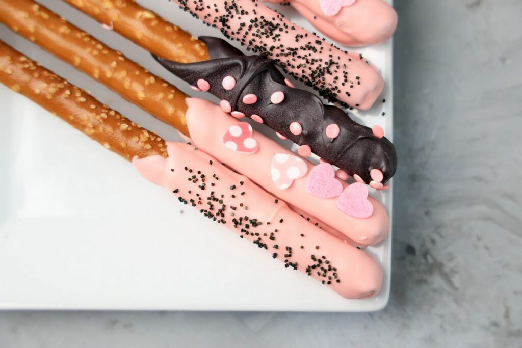 Valentine's Day Pretzel Rods on a white plate on a faux concrete backdrop.