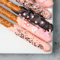 Valentine's Day Pretzel Rods on a white plate on a faux concrete backdrop.