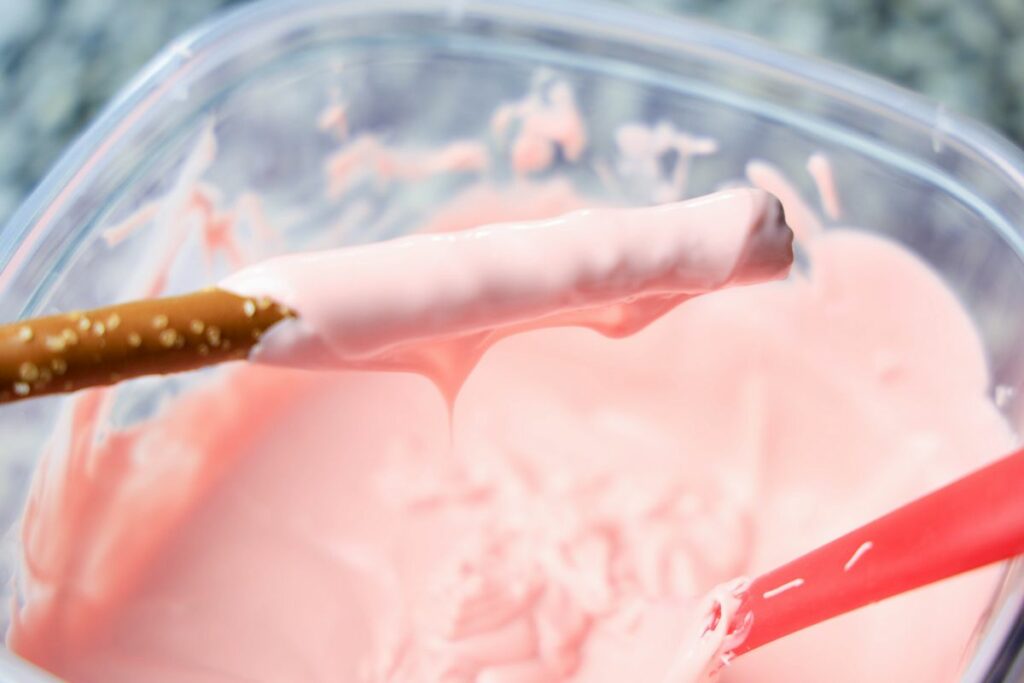 Pink candy melts melted in a bowl with a pretzel rod dipped.