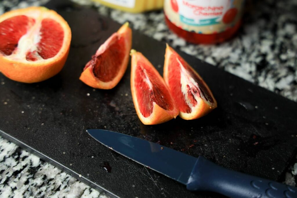 Blood orange cut up on a black cutting board.