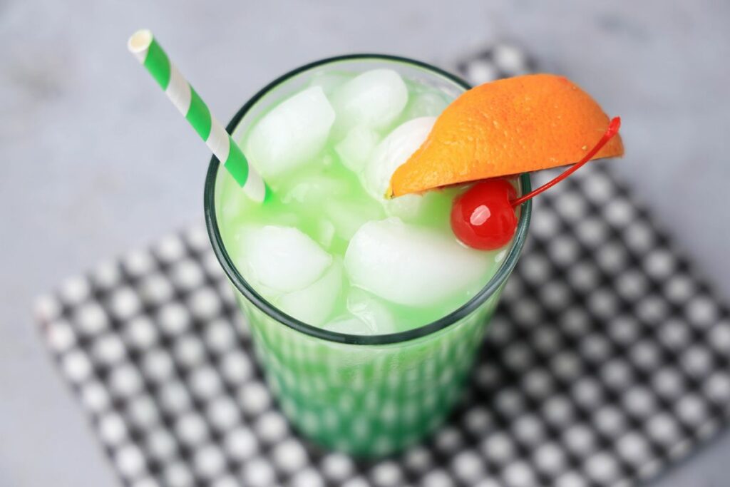 Drunken Leprechaun cocktail with a green striped straw on a gray plaid napkin with a faux concrete backdrop.