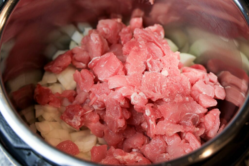 Pork stew meat with diced onions inside the instant pot.