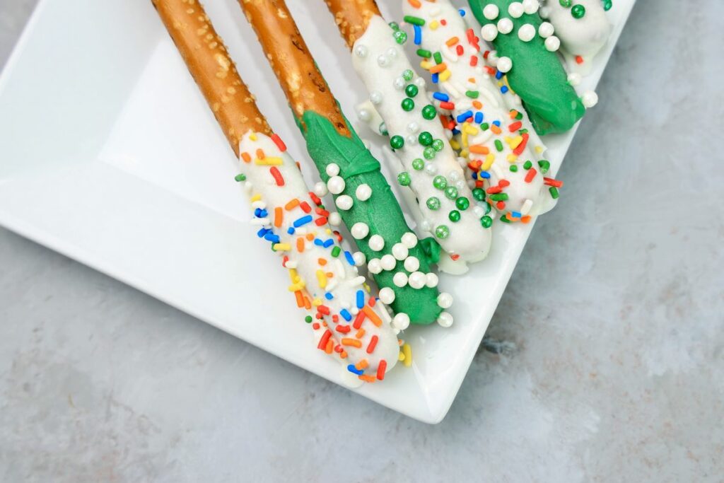 St. Patrick's Day dipped pretzel rods on a white plate on a faux concrete backdrop.