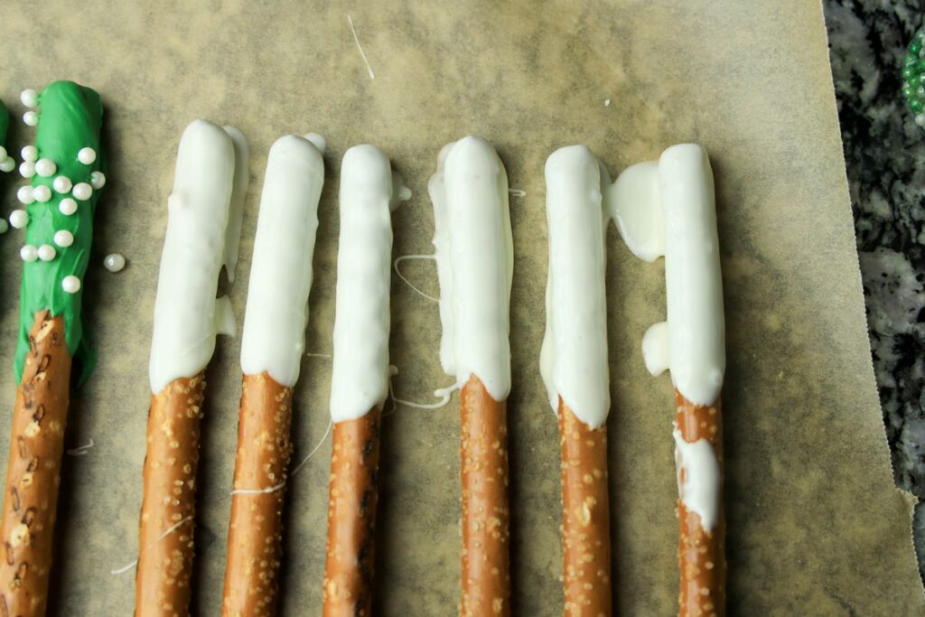 White chocolate dipped pretzel rods on parchment paper.