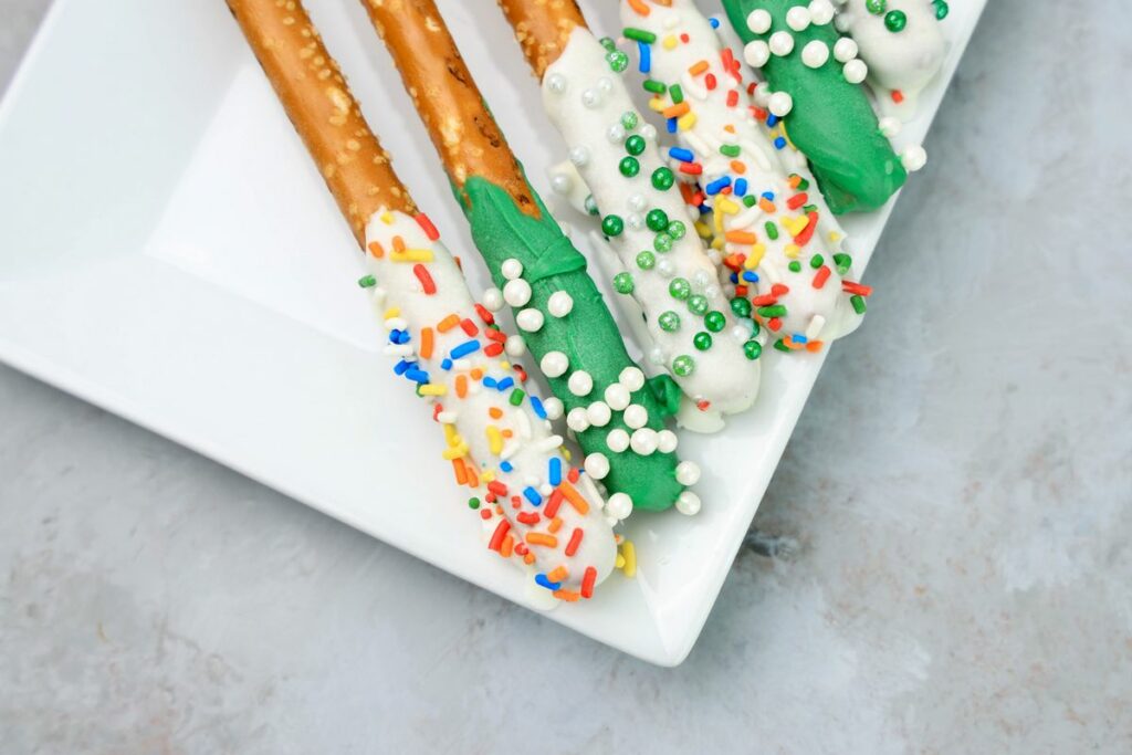 St. Patrick's Day dipped pretzel rods on a white plate on a faux concrete backdrop.