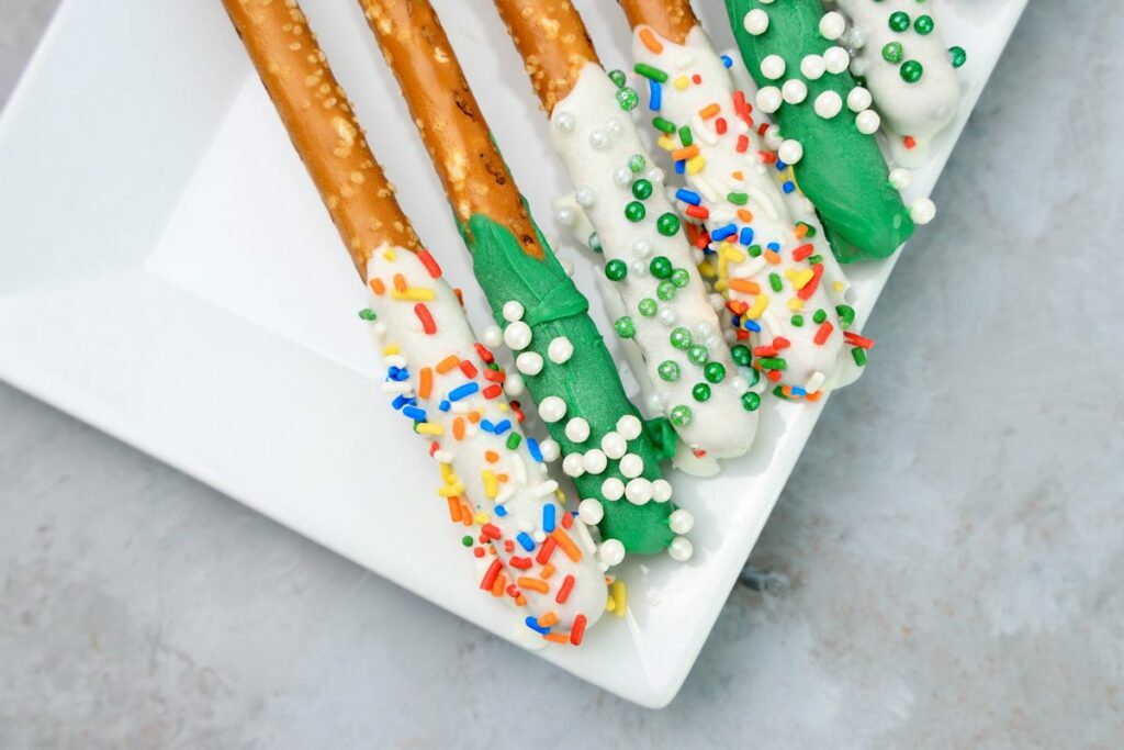 St. Patrick's Day dipped pretzel rods on a white plate on a faux concrete backdrop.