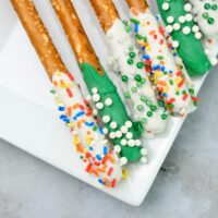 St. Patrick's Day dipped pretzel rods on a white plate on a faux concrete backdrop.