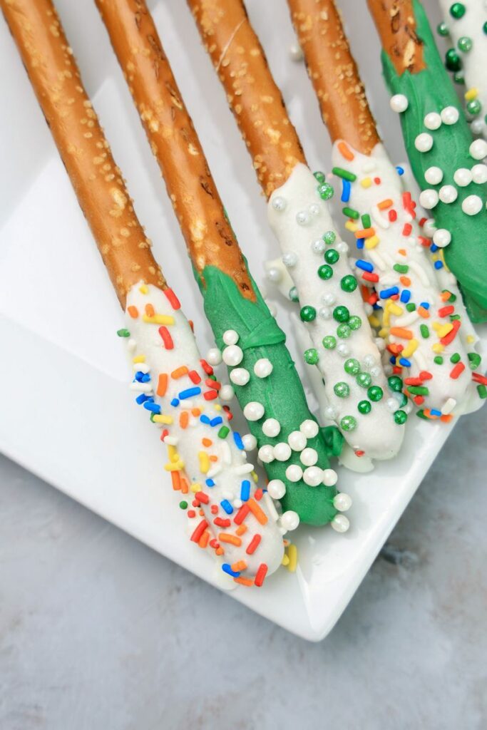 St. Patrick's Day dipped pretzel rods on a white plate on a faux concrete backdrop.