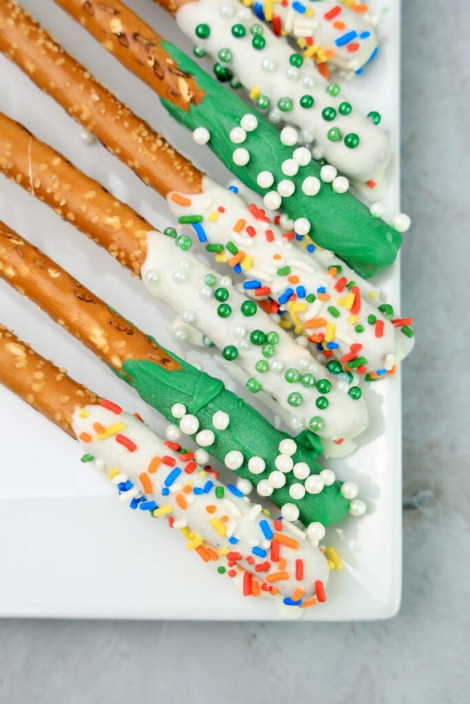 St. Patrick's Day dipped pretzel rods on a white plate on a faux concrete backdrop.