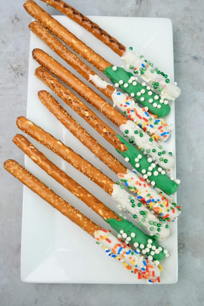 St. Patrick's Day dipped pretzel rods on a white plate on a faux concrete backdrop.