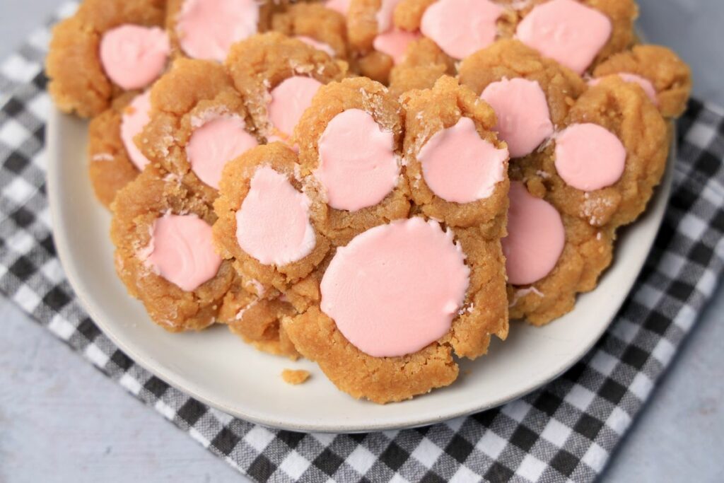 Peanut butter bunny paw cookies with pink candy melts on a white plate with gray plaid napkin.