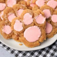 Peanut butter bunny paw cookies with pink candy melts on a white plate with gray plaid napkin.