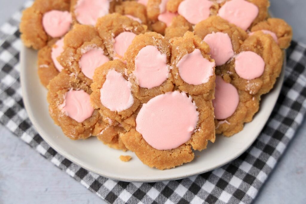 Peanut butter bunny paw cookies with pink candy melts on a white plate with gray plaid napkin.