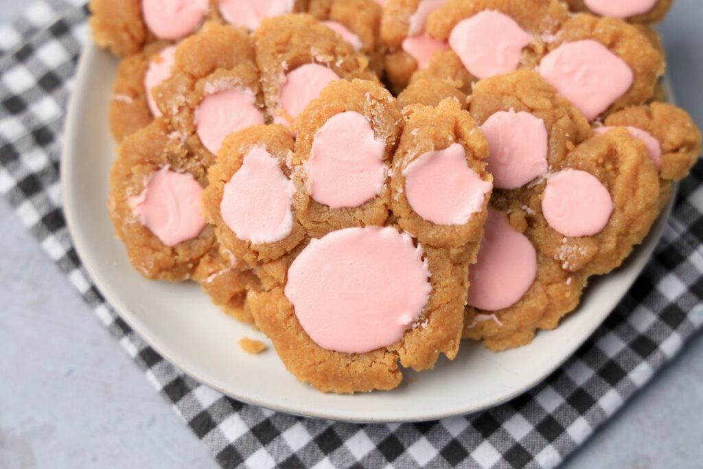 Peanut butter bunny paw cookies with pink candy melts on a white plate with gray plaid napkin.