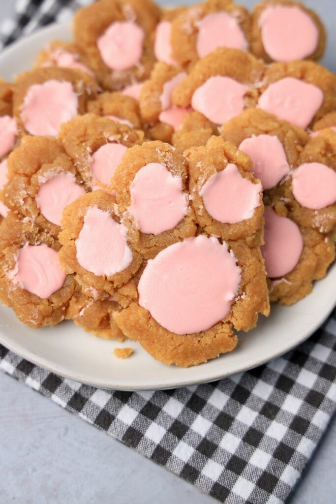 Peanut butter bunny paw cookies with pink candy melts on a white plate with gray plaid napkin.