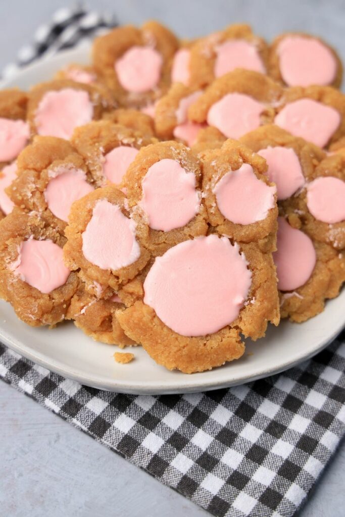 Peanut butter bunny paw cookies with pink candy melts on a white plate with gray plaid napkin.