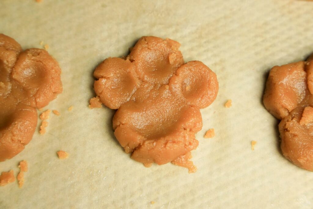 Peanut butter cookie dough pressed into a paw on parchment paper on a baking sheet.