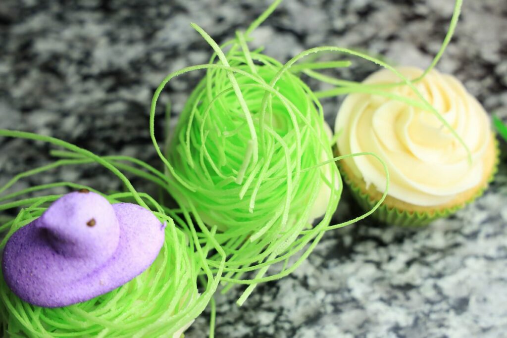 Topping cupcakes with frosting, peeps, and edible grass.