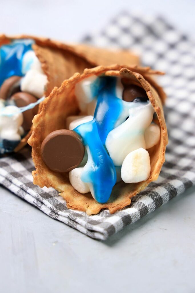 Shark campfire cones loaded with marshmallows, Hershey's kisses, and shark gummy candies.