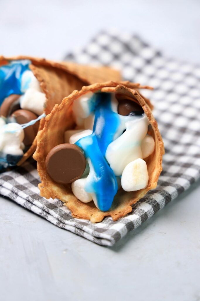 Shark campfire cones loaded with marshmallows, Hershey's kisses, and shark gummy candies.