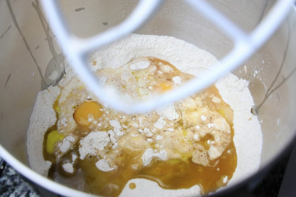 Wet ingredients like egg, apple cider, and milk in a stainless mixing bowl.