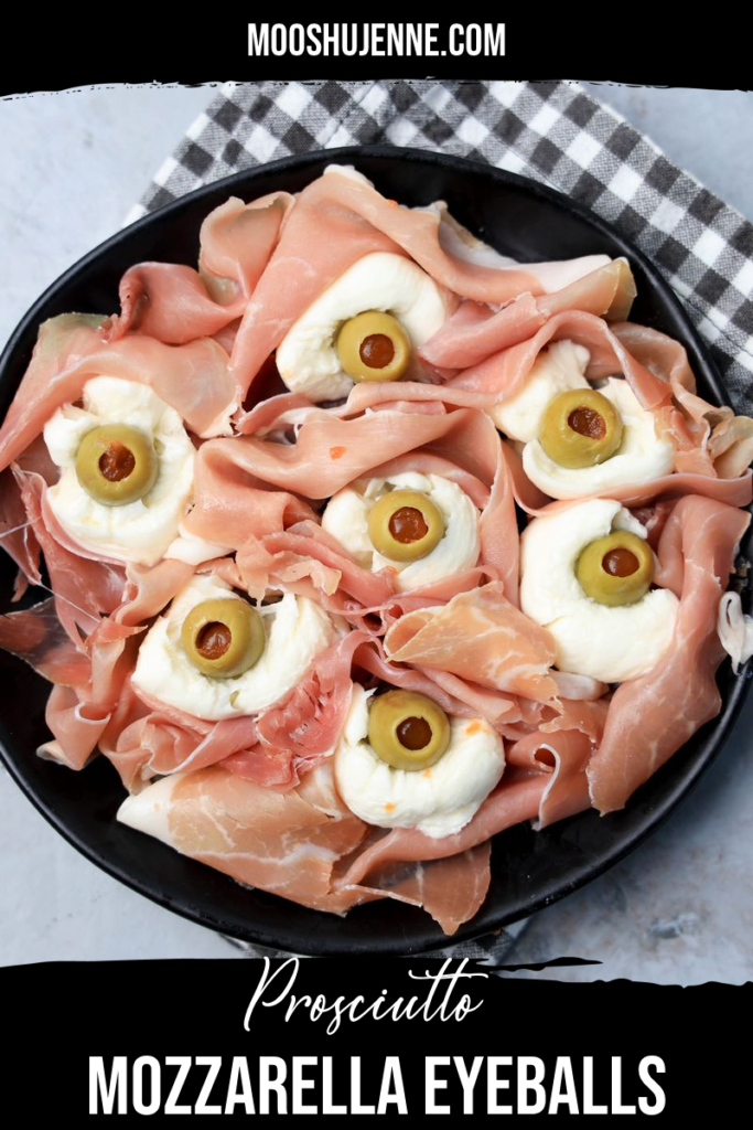 Fresh mozzarella, green olives, and prosciutto to make spooky eyeballs on a black plate.