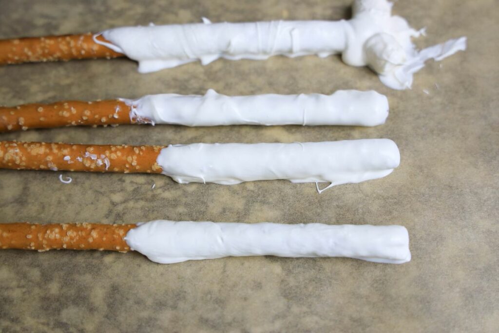 Pretzel rods dipped in white candy melts on parchment paper.